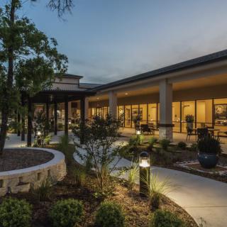 A modern building with outdoor lights illuminating a landscaped patio area during the evening.