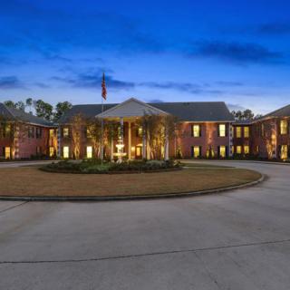 A large, illuminated mansion with a circular driveway at dusk.