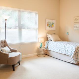 A cozy, minimalist bedroom with a single bed, armchair, and decorative elements.