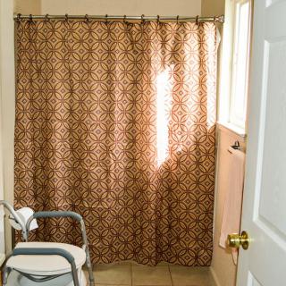 Sunlit bathroom with patterned shower curtain and chair.