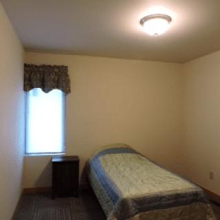 A minimalist bedroom with a single bed and a small nightstand beside a window.