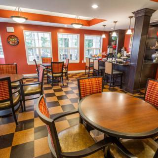 A cozy restaurant interior featuring round and square tables with checkered flooring and warm lighting.