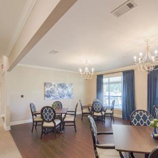A well-lit dining room with elegant chandeliers, multiple tables and chairs, adorned with curtains and a wooden floor.