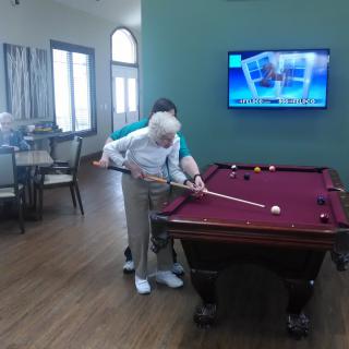 An elderly person receiving help to play billiards in a game room.