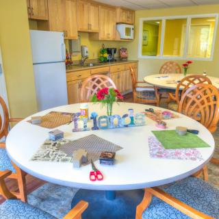 A cozy kitchen and dining area with a round table set up for crafts, featuring scissors, paper, and a decorative 'Friends' centerpiece.