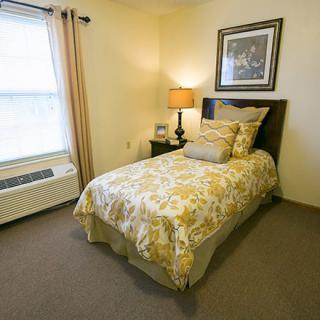 A cozy bedroom with a single bed and decorative bedding, featuring a bedside lamp and framed artwork above the headboard.