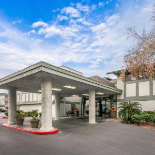 The entrance of a modern building with a covered driveway under a partly cloudy sky.