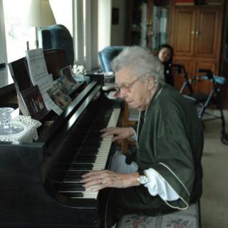 An elderly person playing the piano indoors.