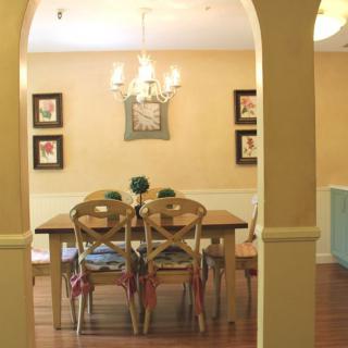 A cozy dining room with a wooden table and chairs, framed by an archway, featuring a chandelier and wall decorations.