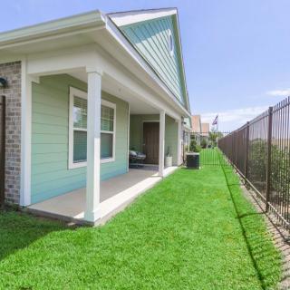 A small house with a well-maintained lawn and porch, bordered by a fence under a clear blue sky.