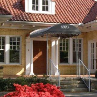 The entrance to a brick house with an awning, steps, and surrounding plants.
