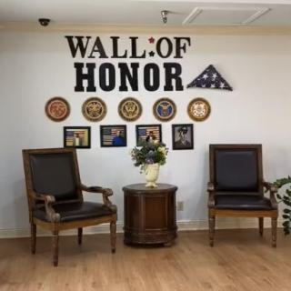 A Wall of Honor display featuring military symbols and plaques, accompanied by wooden chairs and a flag in a decorative setting.