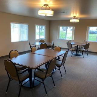 A spacious dining area with multiple tables and chairs, well-lit by overhead lighting and natural light from the windows.