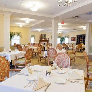 An elegant dining room with neatly arranged tables and chairs, featuring place settings and a chandelier.