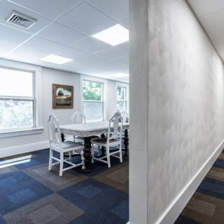 A bright meeting room with white chairs and a table, featuring large windows and artwork on the wall.