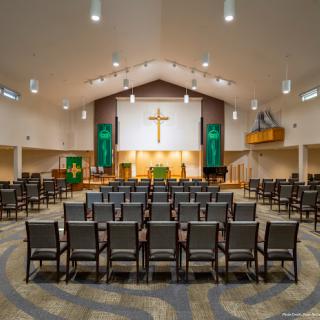 A view of the interior of a modern church sanctuary, featuring rows of chairs and a prominent cross.
