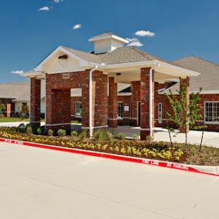 A welcoming entrance to a residential building, featuring brick columns and landscaped gardens under a clear blue sky.