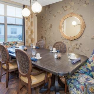 A well-decorated dining room with a large wooden table, elegant chairs, and a stylish mirror on the wallpapered wall.