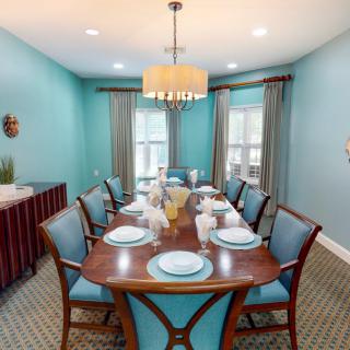 A stylish dining room with turquoise walls, a wooden dining table set for eight, and an elegant chandelier overhead.