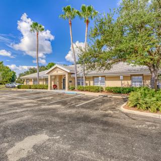 A single-story building with a parking lot surrounded by palm trees and greenery under a bright blue sky with clouds.