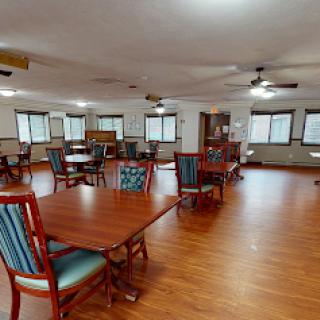 A spacious dining area featuring wooden tables and chairs, illuminated by natural light from multiple windows.