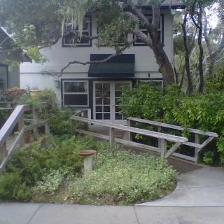 A house with a ramp leading through a garden surrounded by trees and greenery.
