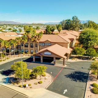 Aerial view of a building surrounded by palm trees and a parking lot on a sunny day.