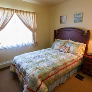 A cozy bedroom with a neatly made bed, floral bedding, and natural light coming through the window.