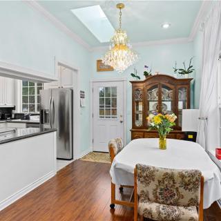 A cozy kitchen and dining area featuring a table set with chairs, an elegant chandelier, and a wooden cabinet, all framed by soft white walls and a skylight.