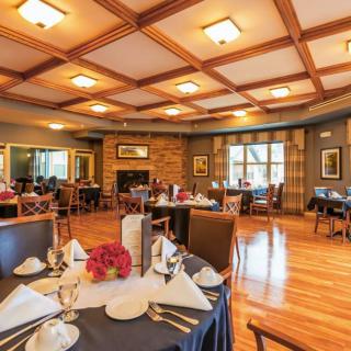 A cozy and elegant restaurant dining room with neatly arranged tables and chairs, featuring wood flooring and warm lighting.