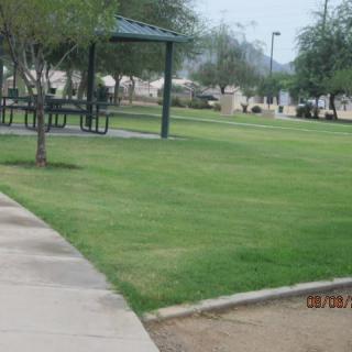 A serene park with a grassy area, trees, a gazebo, and a paved walkway.