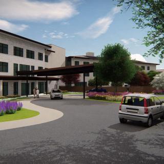A modern building with a circular driveway and landscaped surroundings on a cloudy day.