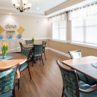 A cozy dining room with several tables and chairs, featuring large windows and elegant decor.