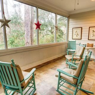 A cozy porch with teal rocking chairs and star decorations, offering a serene nature view through large windows.