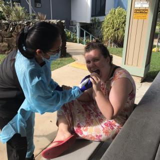 A woman in a floral dress interacts with an animal under the care of a person wearing protective gear.