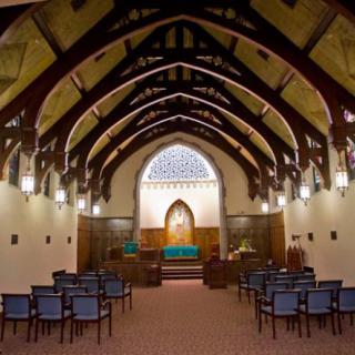 Interior view of a chapel with wooden beams and stained glass.