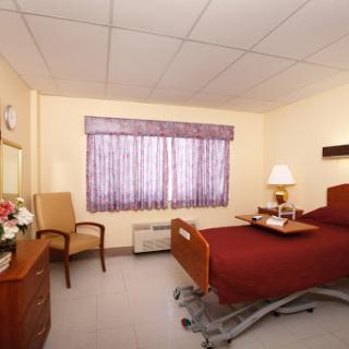 A comfortable hospital patient room featuring a bed, chair, and window with natural light.