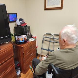An elderly man in a wheelchair enjoying a show on his tablet in a cozy room.