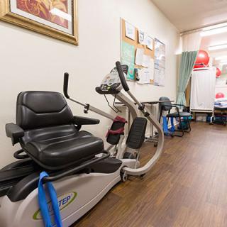A healthcare facility room with exercise equipment, including a recumbent bike used for physical therapy.