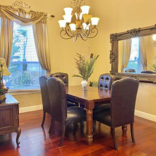 Elegant dining room with a chandelier, large mirror, and a wooden table surrounded by leather chairs.