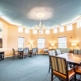 A spacious dining room with multiple tables, chairs, and a chandelier, featuring large windows and soft lighting.