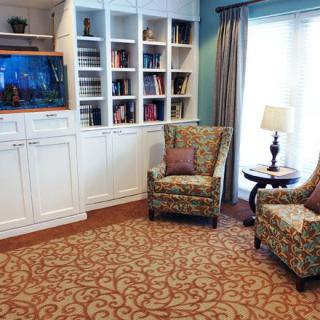 A cozy living room with a bookshelf, comfortable chairs, and a soft carpet.