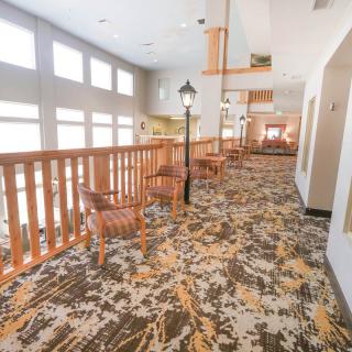 A bright corridor with wooden railings, patterned carpet, and seating areas along the side.