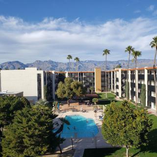 A scenic view of a hotel with a swimming pool, surrounded by palm trees and mountains in the background.