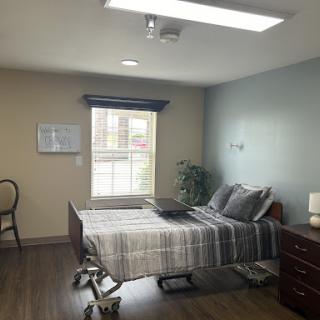 A well-lit hospital room featuring a bed, chair, and minimalistic decor.