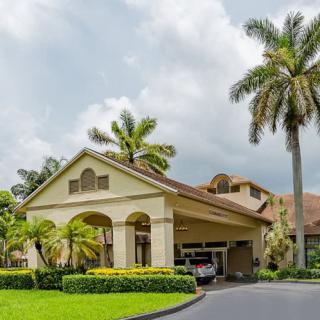 A beautiful house with a covered entrance surrounded by lush landscaping and palm trees under a cloudy sky.
