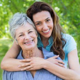 A daughter embraces her mother, both smiling joyfully outdoors.