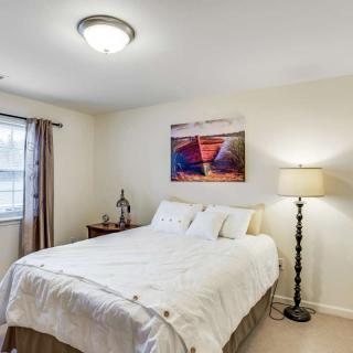 A cozy bedroom with a neatly made bed, artwork on the wall, and warm lighting from a floor lamp.