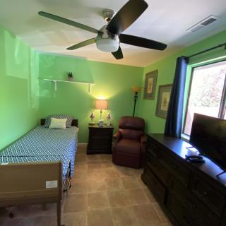 A compact bedroom with bright green walls featuring a single bed, recliner, dresser, and television.