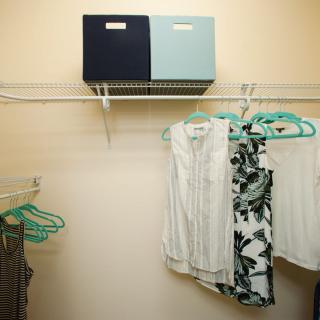 A well-organized closet with clothes hanging on teal hangers and storage boxes on the shelf.